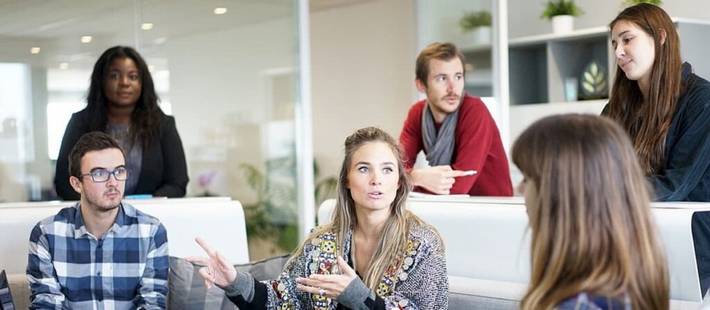 Várias pessoas sentadas em volta de uma mulher que é a chefe da empresa.