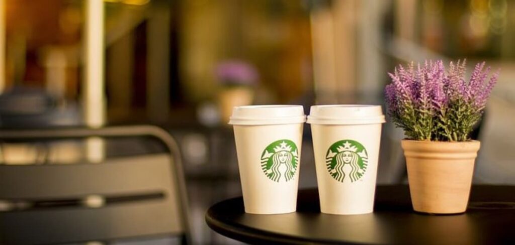 Foto de uma mesa, em cima dela dois copos de café da marca Starbucks.