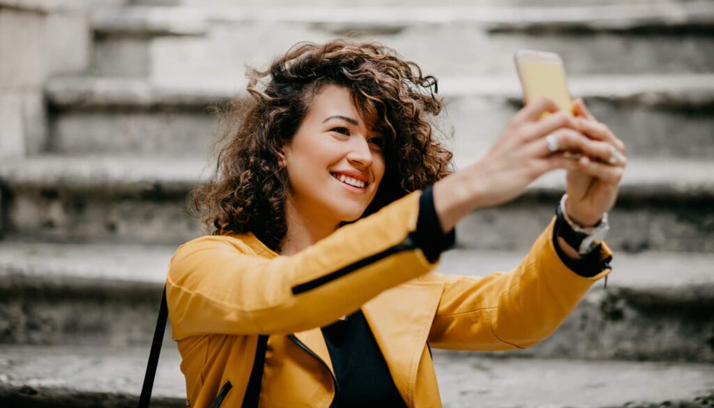 Uma mulher influenciadora segurando seu smartphone tirando uma self.