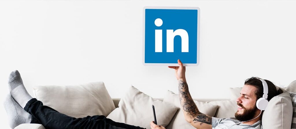 Homem sentado em um sofá segurando o ícone do Linkedin.