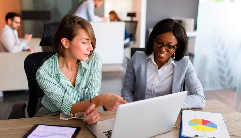 Duas mulheres conversando, uma está apontando para o notebook.