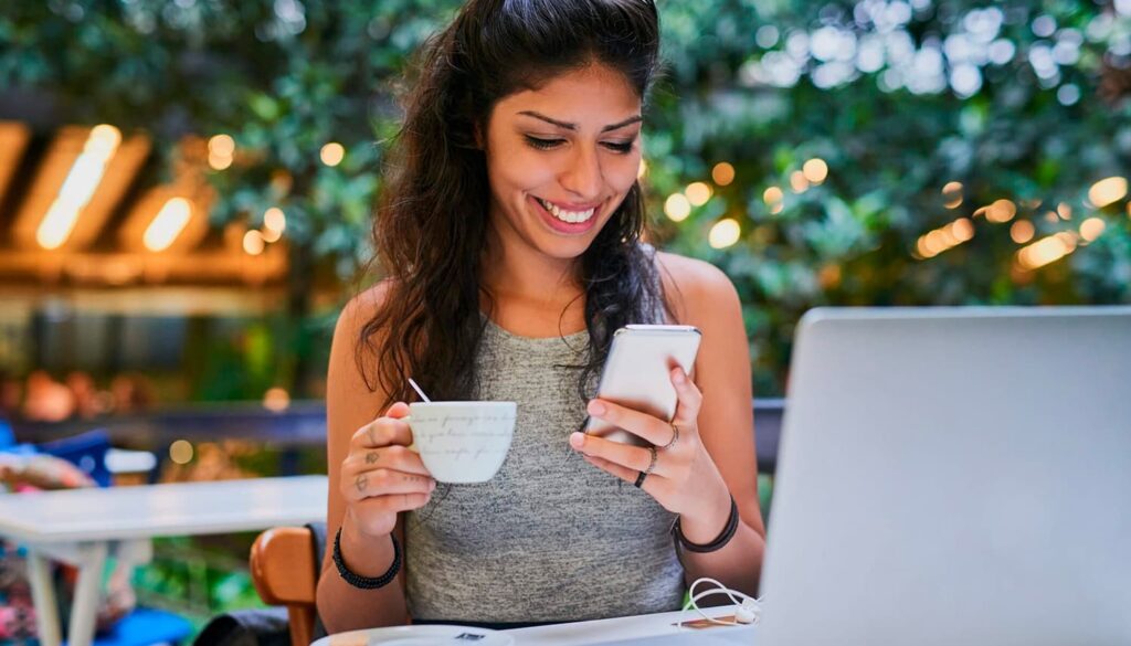 Mulher mexendo em um celular, ela está tomando um café.