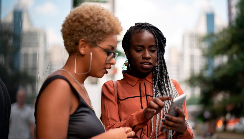 Duas mulheres conversando na rua, uma está mostrando algo no celular para a outra.