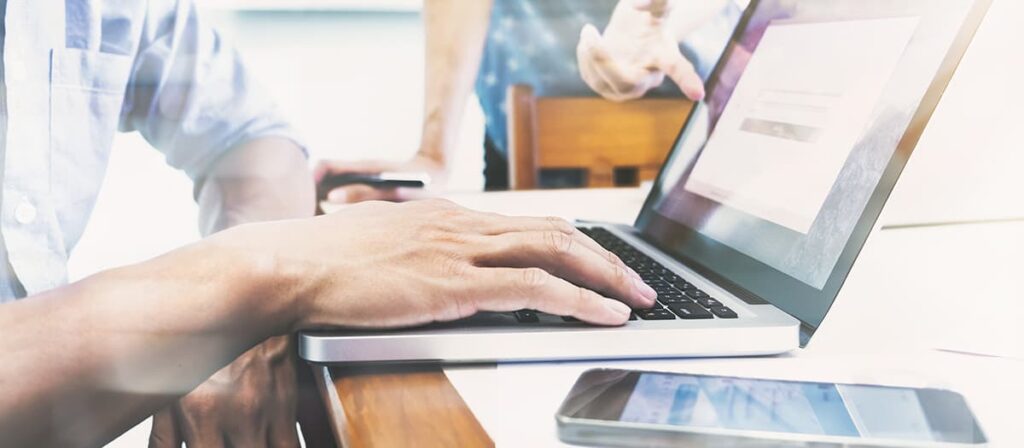 Um homem usando um notebook, outra pessoa está apontando para a tela do notebook.