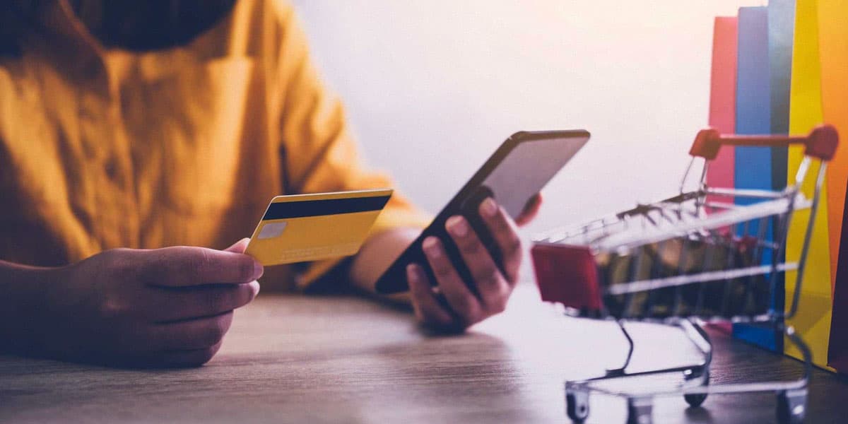 Homem negro segurando um cartão de débito enquanto faz uma compra online.