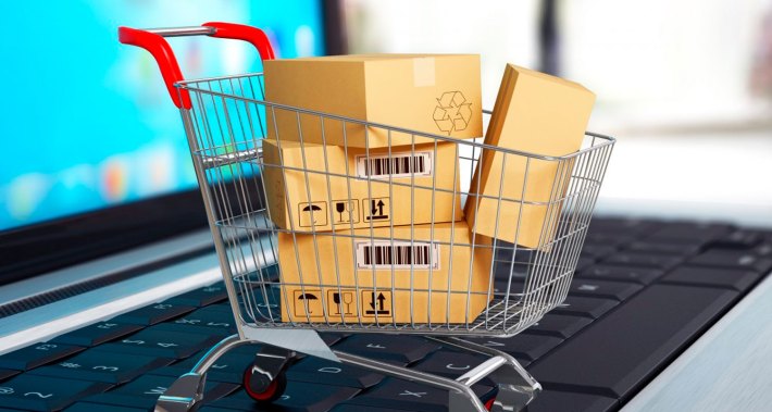 Computador aberto, com carrinho de compra cheio de embalagens de compras.