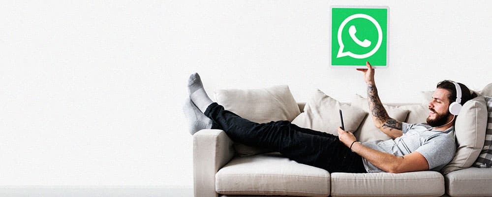 Homem sentado em um sofá segunrando a logo do WhatsApp