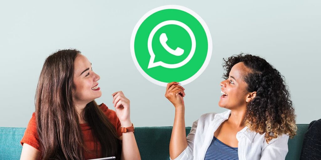 Mulher mulheres sentadas em um sofá uma dela segurando a logo do WhatsApp